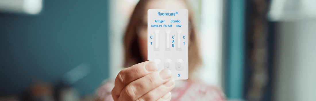Person hält einen fluorecare Antigen Schnelltest mit Anzeige für COVID-19, Flu A/B und RSV vor unscharfem Hintergrund