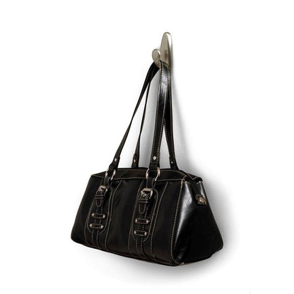 De un cârlig metalic Command™ „clasic” de la 3M Deutschland GmbH este agățată o geantă de mână din piele neagră cu mânere duble și catarame decorative. Geanta are cusături albe și o suprafață ușor lucioasă.