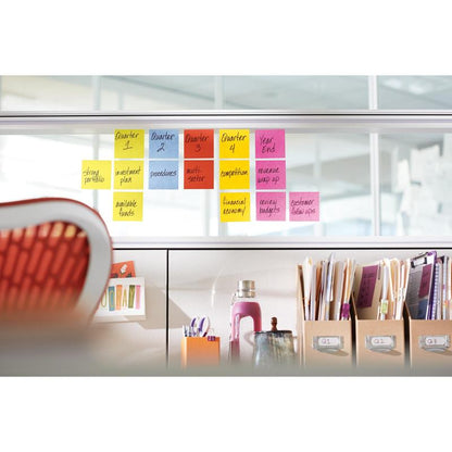 În birou, un perete despărțitor arată sarcinile trimestriale pe Post-it® Super Sticky Z-Notes colorate (76 x 76 mm, 20+4 blocuri) de la 3M, în fața cărora se află un scaun portocaliu și rafturi cu sticle, dosare și mape.