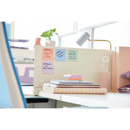 Un birou ordonat cu un teanc de caiete, un bloc 3M Post-it® Super Sticky Z-Notes Boost Collection, o sticlă de apă cu capac alb, o lampă și rafturi în fundal. Lumina soarelui pătrunde prin ferestre mari.