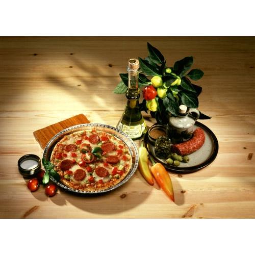 O pizza cu peperoni se află pe o farfurie lângă vin alb, cârnați și măsline – proaspăt coaptă în Starpak 25 Rundformen Alu rund de la Starpak pentru o conducere optimă a căldurii – însoțită de roșii, ardei și o plantă în ghiveci pe o masă din lemn.