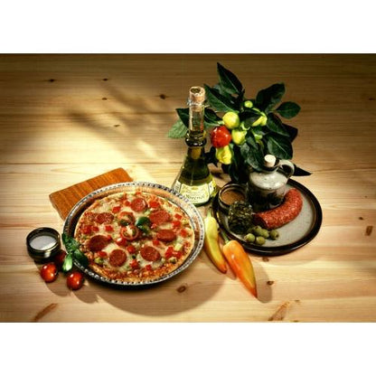 O pizza cu peperoni se află pe o farfurie lângă vin alb, cârnați și măsline – proaspăt coaptă în Starpak 25 Rundformen Alu rund de la Starpak pentru o conducere optimă a căldurii – însoțită de roșii, ardei și o plantă în ghiveci pe o masă din lemn.