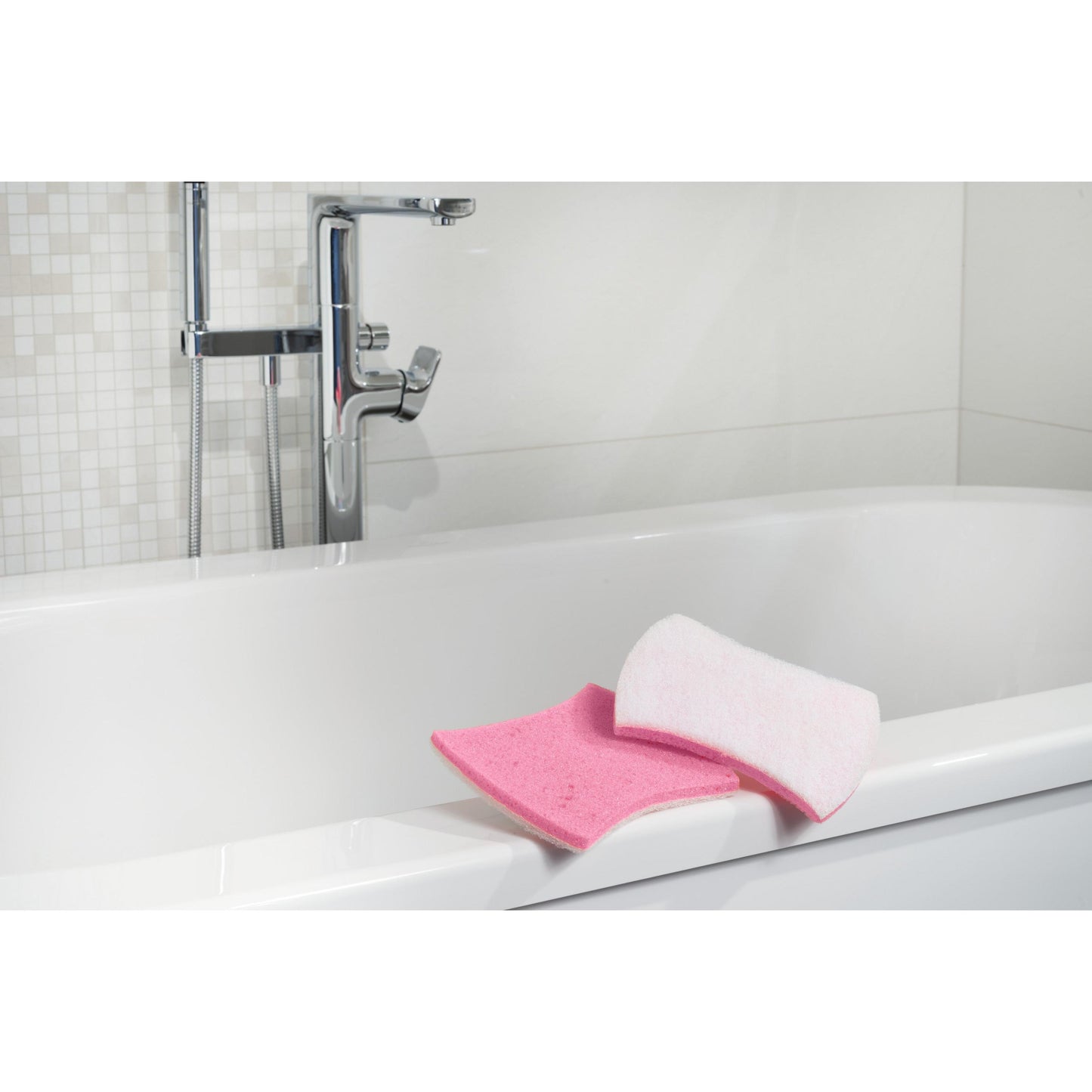 Gezeigt wird eine weiße Badewanne mit verchromten Armaturen. Am Rand befinden sich ein rosa Badezimmerschwamm und ein Scotch-Brite® Bath XXL Reinigungsschwamm für das Bad von 3M Deutschland GmbH. Der Hintergrund zeigt weiße Fliesen mit Mosaikmuster.