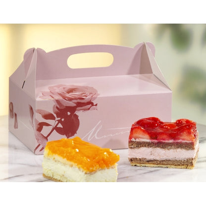 O cutie de patiserie PAPSTAR 15, carton pătrat roz cu mâner de la PAPSTAR GmbH stă pe marmură. În fața ei sunt două felii de prăjitură: una cu topping portocaliu, cealaltă cu topping de căpșuni roșii.