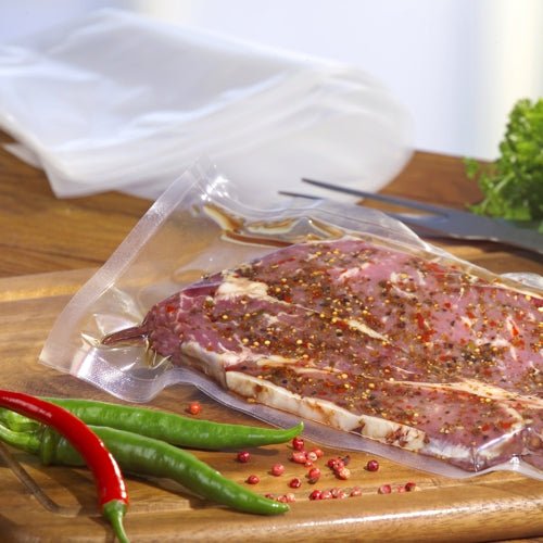 Un plic Starpak 100 cu margine sigilată, PA / PE transparent, umplut cu carne marinată, se află pe un tocător de lemn cu ardei iuți întregi și boabe de piper împrăștiate în apropiere, capturând o scenă proaspătă de vidare a alimentelor de la Starpak.