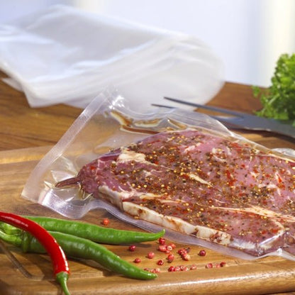 Un plic Starpak 100 cu margine sigilată, PA / PE transparent, umplut cu carne marinată, se află pe un tocător de lemn cu ardei iuți întregi și boabe de piper împrăștiate în apropiere, capturând o scenă proaspătă de vidare a alimentelor de la Starpak.