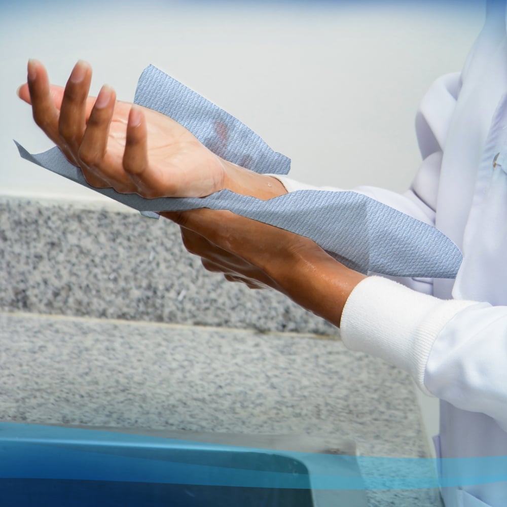 O persoană într-un halat alb își usucă mâinile cu prosoape Scott® - rolă (304,00 m x 19,80 cm) de la Kimberly-Clark GmbH de pe o rolă de prosoape de hârtie lângă un blat de granit și o chiuvetă.