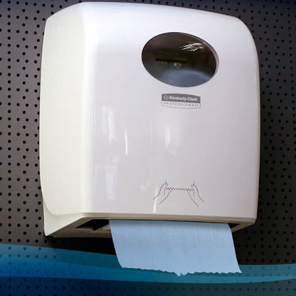 Un distribuitor alb montat pe perete de la Kimberly-Clark GmbH ține o rolă de prosoape Scott® (304,00 m x 19,80 cm) cu un prosop albastru și o instrucțiune simplă, ilustrată, pe un fundal întunecat din tablă perforată.