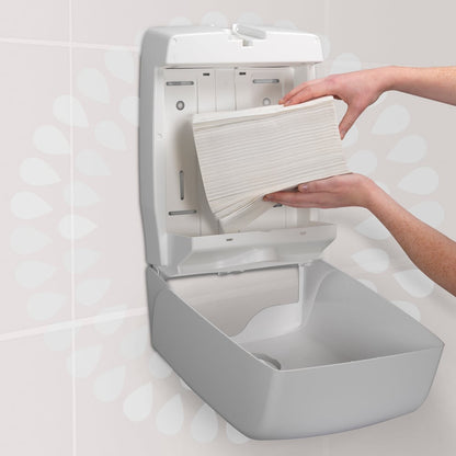 O persoană încarcă un teanc de șervețele de mână Kleenex® Ultra™ MultiFold de la Kimberly-Clark GmbH (alb, mic, 18 pachete x 150 foi) într-un dispenser de șervețele de hârtie montat pe perete într-o toaletă.