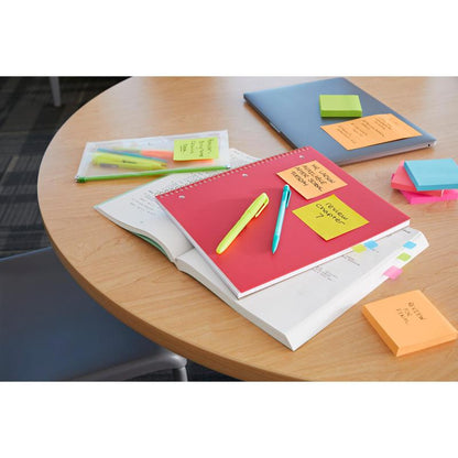 O masă rotundă din lemn cu un caiet roșu, un manual deschis, pixuri, markere, un laptop, o mapă de plastic transparent și 3M Deutschland GmbH Post-it® Super Sticky Z-Notes (Boost Collection, 76x76mm) este vizibilă; un scaun este parțial ilustrat.