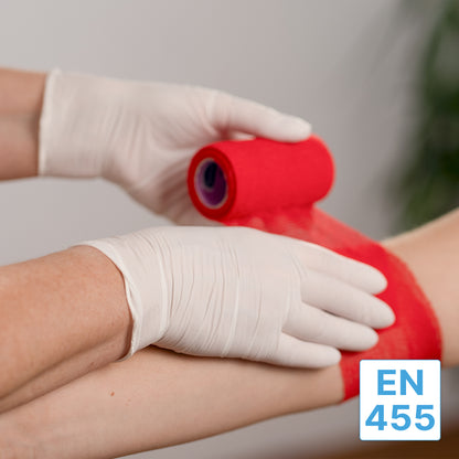 Eine Person, die ARNOMED NITRIL WHITE 200er Nitrilhandschuhe von ARNOWA GmbH trägt, wickelt einer anderen Person eine rote Bandage um den Arm. In der rechten unteren Ecke ist ein blau-weißes "EN 455"-Etikett zu sehen.