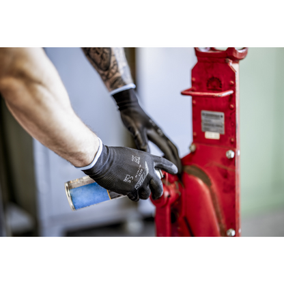 O persoană cu mănuși din nailon NITRAS, negre, acoperite cu PU de la AS Arbeitsschutz GmbH curăță sau unge cu un spray albastru o piesă roșie de mașină din metal. Se văd doar brațele și mâinile.