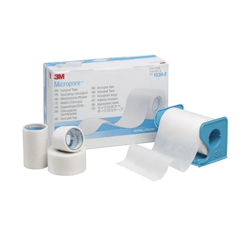 Imaginea arată un plasture 3M Healthcare Germany GmbH 3M-Medica Micropore, culoarea pielii – 12 bucăți | Cutie (12 bucăți) cu plasturi de diferite dimensiuni în fața ei. Un rolă de plasture se află într-un distribuitor albastru, în timp ce alte două role de plasture și o rolă mai mică stau vertical lângă cutie. Plasturele hipoalergenic este alb.