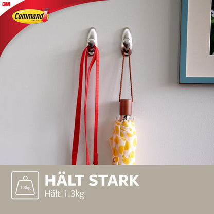 Două cârlige metalice Command™ „clasic” de la 3M Deutschland GmbH sunt montate pe un perete alb și susțin o lesă roșie și o umbrelă cu model galben. Textul spune: „ȚINE PUTERNIC Ține 1.3kg” și arată logo-ul Command.