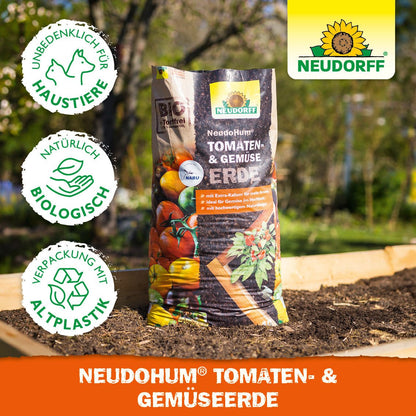 Un sac de NeudoHum Tomaten- & GemüsesErde din Neudorff Shop se află pe un strat de grădină, cu simboluri pentru protecția animalelor, calitate bio și ambalaj din plastic reciclat. Logo-ul Neudorff este situat în colțul din dreapta sus.