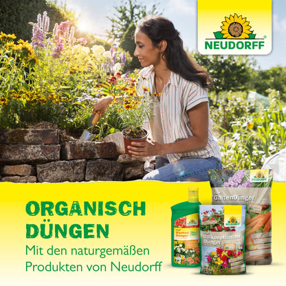 Eine Frau kniet in einem Garten und pflanzt Blumen an einer Steinmauer. Im Vordergrund stehen die Azet Düngesticks für Tomaten & Erdbeeren von Neudorff Shop mit dem Sonnenblumenlogo und dem deutschen Werbetext.