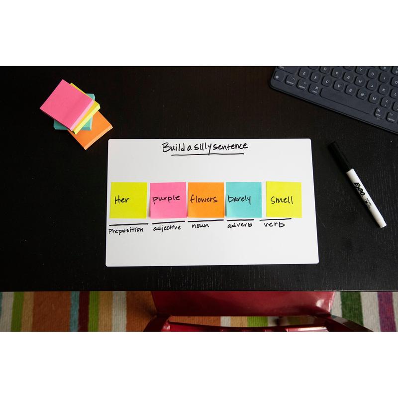 Un cub de note Post-it® al 3M Deutschland GmbH (76x76mm, 450 foi, 100% PEFC) arată un exercițiu de construcție a propozițiilor pe un tablă albă cu etichete gramaticale; note adezive suplimentare, un marker, o tastatură și un covor dungat sunt în apropiere.