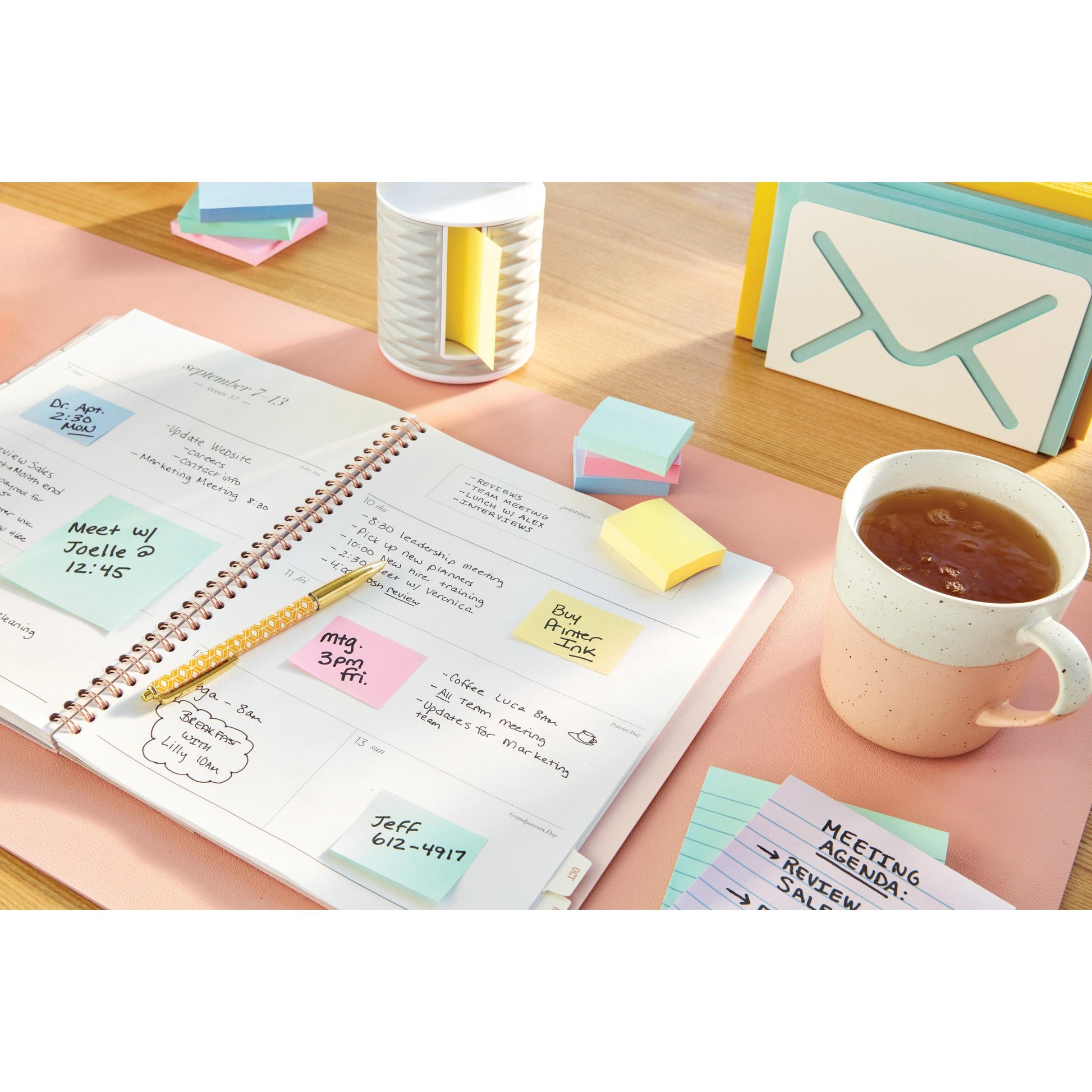Ein offener Planer mit handschriftlichen Notizen, Karteikarten, einem Bleistift, Büromaterial und einer Tasse Tee liegt auf einem Holztisch. Eine Packung 3M Post-it® Notes Gelb 38x51 mm (8 Blöcke + 4 Gratis/Packung) ist ebenfalls zu sehen.