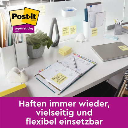 O masă de birou modernă cu laptop, planificator, plantă, suport pentru bandă adezivă și materiale de birou arată mai multe notițe galbene Post-it® Super Sticky de la 3M Deutschland GmbH (76 mm x 76 mm, 45 foi/bloc, 100% PEFC) atașate la obiecte. Text german într-un banner mov dedesubt.