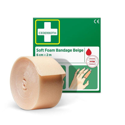 Un rulou de bandaj din spumă moale Cederroth bej (6 cm x 2 m) de la Orkla Wound Care AB este prezentat în fața ambalajului său verde-alb cu instrucțiuni ilustrate și un simbol cu picătură roșie.