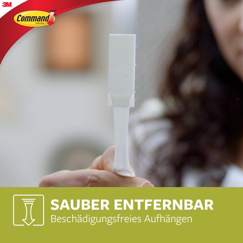 O persoană ține o bandă albă de montare pentru imagini Command™ L de la 3M Deutschland GmbH (6 seturi, pachet avantajos, 17206-6). Imaginea arată logo-ul Command și textul: "Îndepărtare curată. Agățare fără deteriorare."