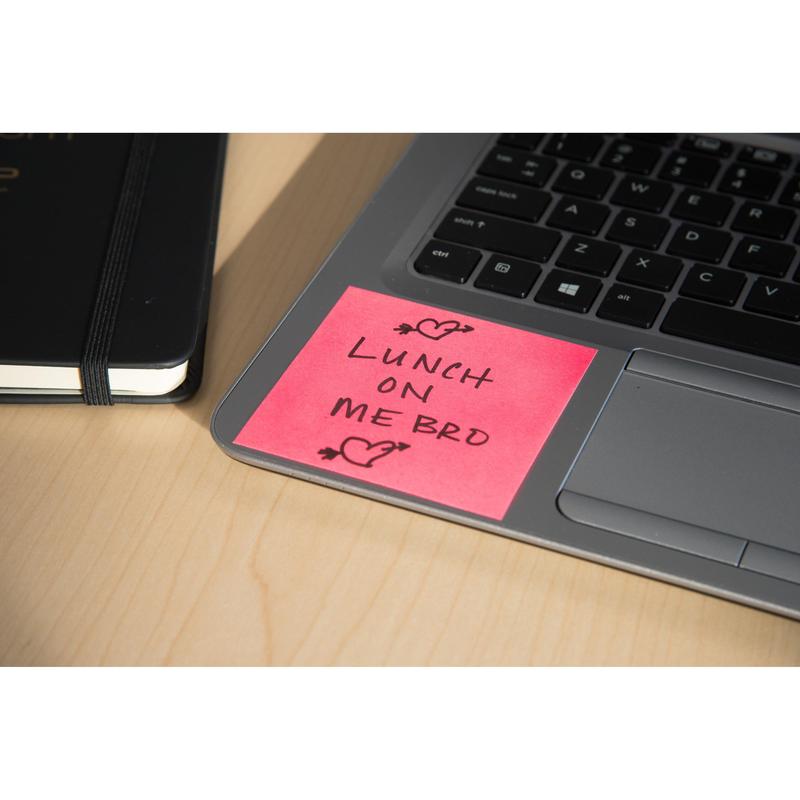 Un cub de note Post-it® (76x76mm, 450 foi, 100% PEFC) de la 3M Deutschland GmbH în roz stă pe o tastatură de laptop cu "LUNCH ON ME BRO" și mâzgălituri de inimă. Un caiet negru închis se află lângă el pe o masă de lemn deschis.