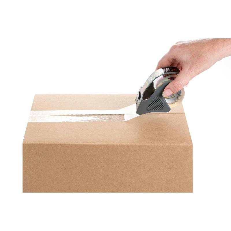 O mână sigilează un carton maro peste cusătura superioară cu bandă adezivă de ambalare Scotch® Box Lock™ 48 mm x 20,3 m de la 3M Deutschland GmbH cu un distribuitor de bandă, totul pe un fundal alb.