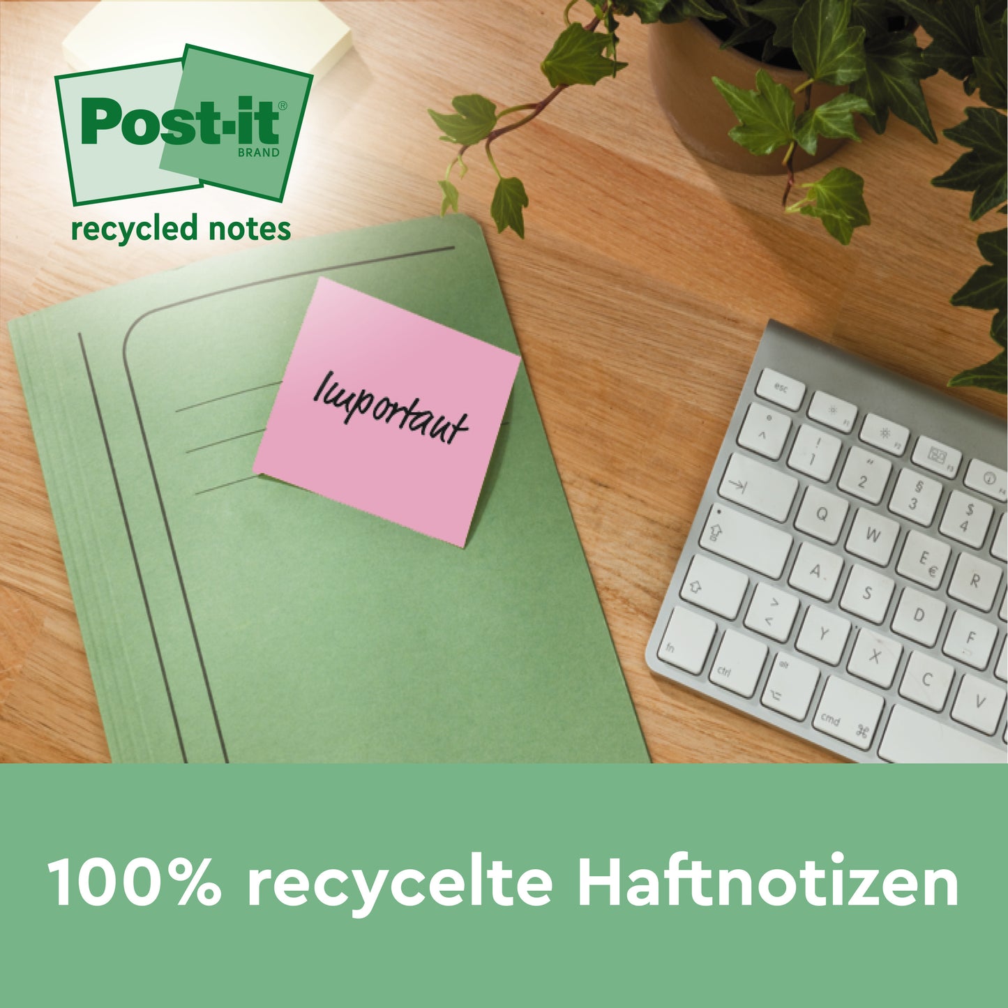 Ein pinkfarbener Post-it® Recycling-Zettel (76 x 127 mm, 100 Blatt, 100% PEFC) der 3M Deutschland GmbH mit der Aufschrift "wichtig" ist an einem grünen Ordner auf einem Holzschreibtisch neben einer Tastatur und einer Pflanze befestigt. Text: "100% recycelte Haftnotizen.