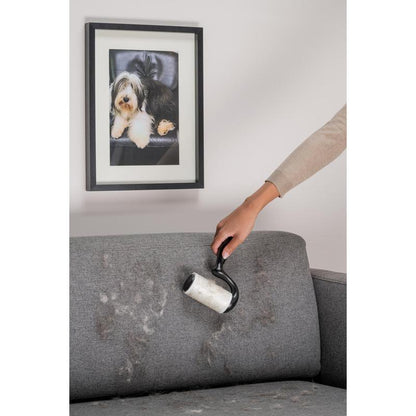 Cu roleul de scame Scotch-Brite™ Everyday Clean pentru suprafețe plane (56 de foi, 1/pachet) de la 3M Deutschland GmbH, cineva îndepărtează părul de animale de pe o canapea de stofă gri, sub o fotografie a unui câine.