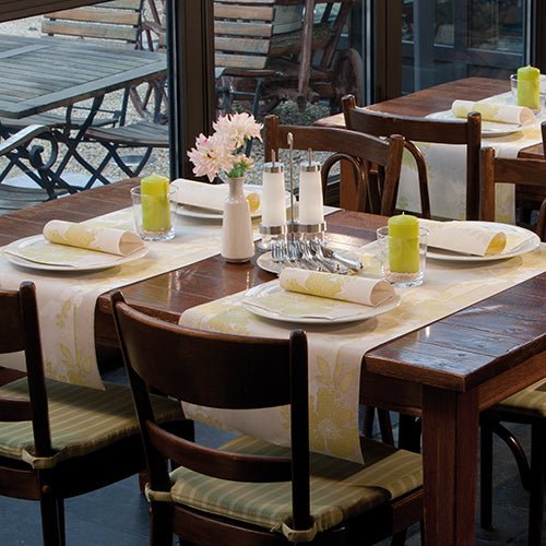 O masă de dining din lemn pentru patru persoane cu farfurii albe, PAPSTAR 50 șervețele "ROYAL Collection" 1/4 pliere 40 x 40 cm verde de la PAPSTAR GmbH, lumânări verzi, veselă de sticlă, solnițe și o vază cu flori roz la fereastră.