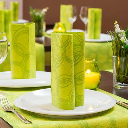 O masă de dining cu farfurii albe, PAPSTAR GmbH 50 șervețele "ROYAL Collection" 1/4 pliere 40x40 cm verde în picioare, tacâmuri de argint, pahare de vin, vaze de flori și lumânări votive verzi pe un alergător verde pentru ocazii festive.