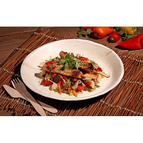 Frigărui de pui la grătar cu o tigaie colorată de legume sunt servite pe o farfurie PAPSTAR 6, frunză de palmier „pure“ rotundă de la PAPSTAR GmbH – veselă ecologică, prezentată cu stil pe un suport țesut cu tacâmuri din lemn și ardei proaspăt în vedere.