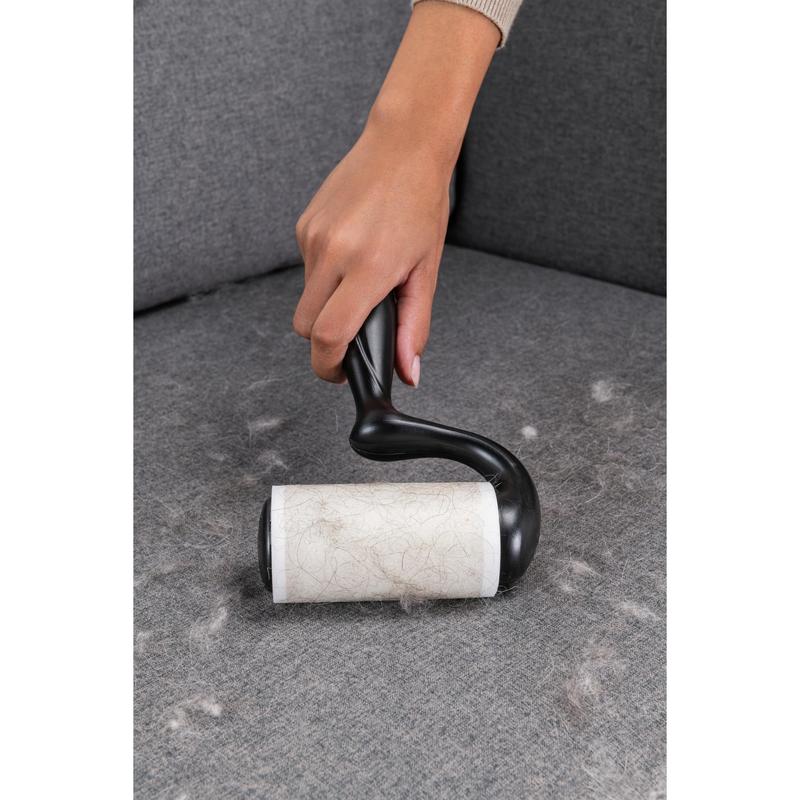 O mână folosește roleul de scame Scotch-Brite™ Everyday Clean pentru suprafețe plane, 56 de foi (3M Deutschland GmbH), pentru a îndepărta părul de animale de pe o canapea gri și pentru a menține suprafețele curate.