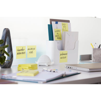 Ein aufgeräumter Bürotisch mit Ordnern, 3M Post-it® Super Sticky Z-Notes, Gelb (76 mm x 76 mm), einer Schildkrötenfigur, einer Pflanze, Stiften, einem geschlossenen Laptop und Papieren. Die Notizen auf den Ordnern lauten "Leistungsüberprüfung" und "Risiko minimieren".