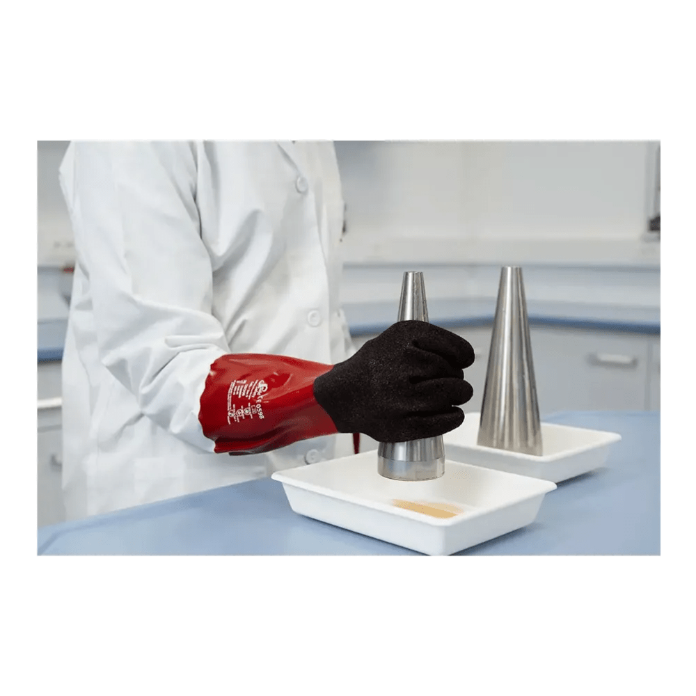 O persoană în halat de laborator și mănuși de protecție chimică roșii AMPri SolidSafety Chem MaxGrip M - L ține cu grijă un con metalic deasupra unui bol alb. Un bol identic cu propriul con metalic se află alături pe masa de laborator albastră, asigurând protecția împotriva acizilor pe parcursul întregului experiment.