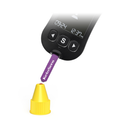 Un dispozitiv digital cu un afișaj „09:24“ și „12:37 Uhr“ este utilizat pentru a testa o bandă violetă cu inscripția „Alphacheck KetoSens β-solutie de control cetonă L+M | Pachet (2 sticluțe)“. Banda Alkacheck Alphacheck KetoSens β-solutie de control cetonă L+M | Pachet (2 sticluțe) indică un mic capac galben. Dispozitivul dispune de un buton mare „S“ sub afișaj.