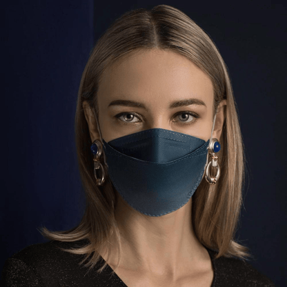 O persoană cu părul lung poartă o mască de față Altruan cu filtru de particule în albastru, care oferă protecție eficientă conform standardului FFP2. O combină cu cercei mari decorativi pe un fundal întunecat și poartă o cămașă neagră.