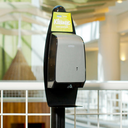 Un suport electronic de loțiuni de spălat Kimberly-Clark GmbH (negru, 1 distribuitor) este amplasat în interior, lângă o balustradă metalică albă, pentru curățarea igienică a mâinilor, cu detalii arhitecturale neclare în fundal.