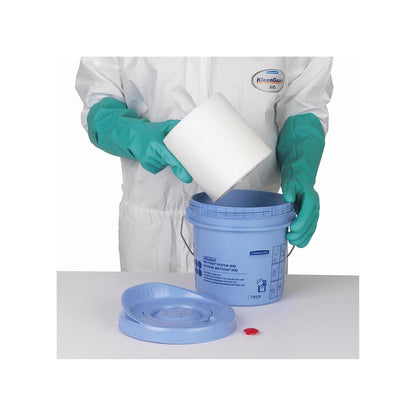 O persoană cu mănuși verzi și costum alb introduce un rulou de șervețele Kimtech® Wettask™ într-o găleată distribuitoare albastră de la Kimberly-Clark GmbH; capacul și dopul roșu sunt așezate pe masă alături.