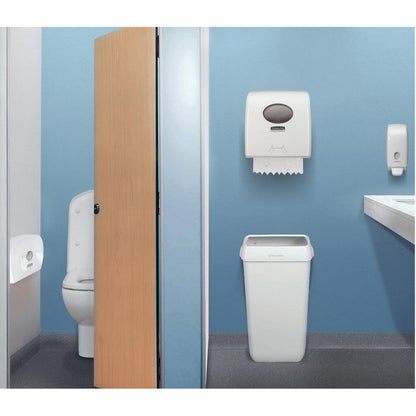 Eine öffentliche Toilette mit Toilettenkabine, blauer Wand, Abfalleimer, Papierhandtuchspender mit Hostess™ NATURA Toilettenpapier (Einzelblattsystem) von Kimberly-Clark GmbH, Seifenspender, Waschbecken und Spiegel.