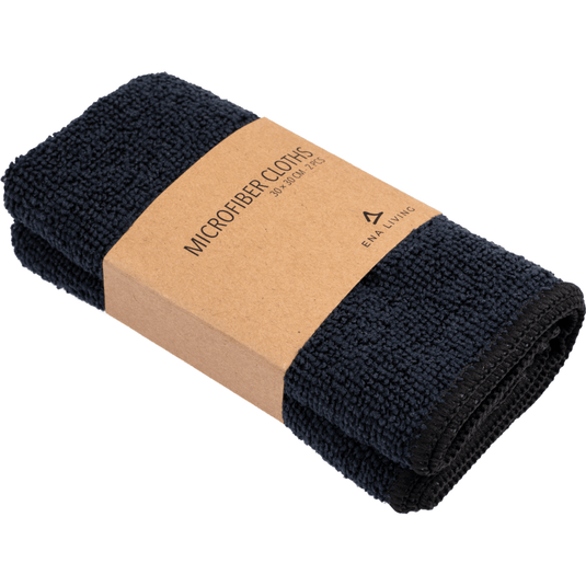 Un set format din două cârpe din microfibră ENA Living de culoare neagră (30x30 cm) de la Abena Re-Seller GmbH, fiecare pliată și prevăzută cu o etichetă maro pe care scrie „Microfiber Cloths 30 x 30 cm” și un logo minimalist – ideale pentru a fi folosite ca cârpe de curățenie în gospodărie.