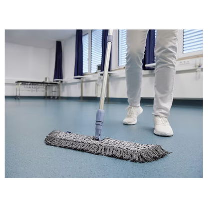O persoană în pantofi și pantaloni albi șterge un podea albastră cu un mop Vileda GmbH Professional Swep Duo r-MicroCombi - 50 cm, într-o cameră cu jaluzele închise și perdele albastre. În apropiere se află o masă pliantă și un calorifer sub ferestre.