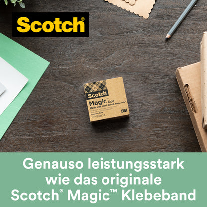 Suportul de birou negru Scotch® C38 cu 3 role de bandă adezivă Scotch® Magic™ (19 mm x 33 m, 66% adeziv pe bază de plante) de la 3M Deutschland GmbH se află pe o suprafață de lemn lângă hârtie, un stilou și un carton.