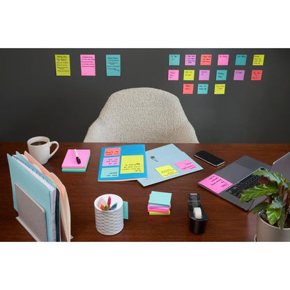 Un birou ordonat cu laptop, cafea, pixuri și rechizite de birou se află în fața unui perete acoperit cu rânduri de 3M Deutschland GmbH Post-it® Super Sticky Notes (47,6mm x 47,6mm, 90 foi/bloc, 100% PEFC); un scaun gol se află în spatele biroului.
