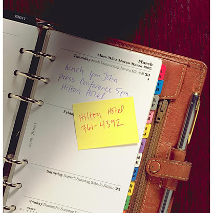 Un planificator legat în piele deschis arată notițe scrise de mână pentru joi: „Prânz 13:00 John”, „Conferință de presă 17:00 Hotel Hilton”. Pe un bloc galben Post-it® Recycling Notes de la 3M Deutschland GmbH scrie: „Hotel Hilton 761-4392”. Separatoarele sunt vizibile.