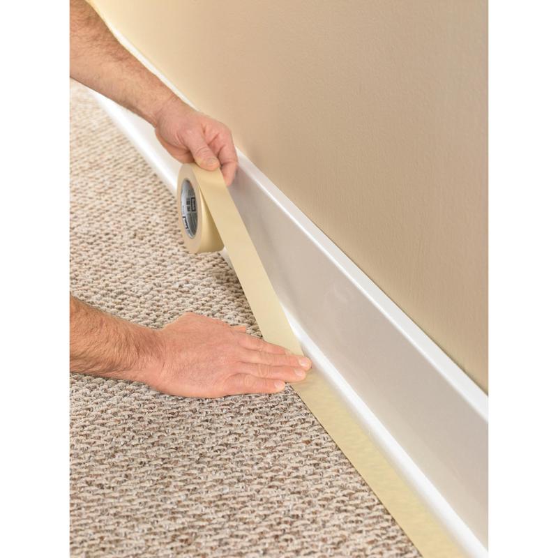 O persoană folosește banda de mascare Scotch® Classic, 24 mm x 50 m (70% PEFC) de la 3M Deutschland GmbH, pentru a lipi plinta unde covorul întâlnește peretele, pentru a proteja finisajul în timpul lucrărilor de vopsire și renovare.