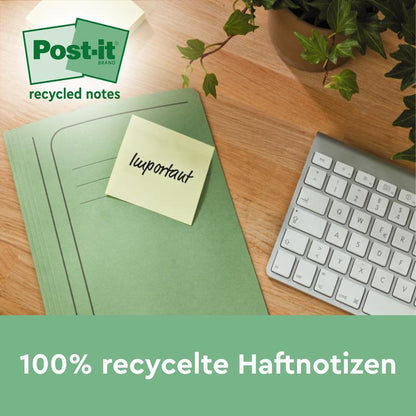 Un dosar verde cu un Post-it® Notes de reciclare galben, 76x127mm, 100 foi/bloc de la 3M Deutschland GmbH este așezat pe un birou de lemn lângă o tastatură albă și o plantă. Notițele sunt 100% PEFC (SGSCH-PEFC-COC-110078) și ecologice.