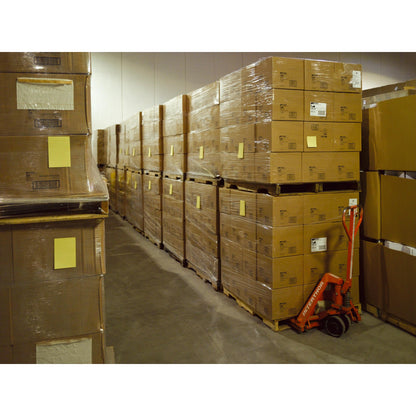 Într-un depozit sunt stive de notițe Post-it® Super Sticky în format mare, Ultra Galben (101 x 152 mm, 90 de foi/bloc, 6 blocuri), de la 3M Deutschland GmbH, ambalate pe paleți. Un transpalet roșu se află lângă ele.