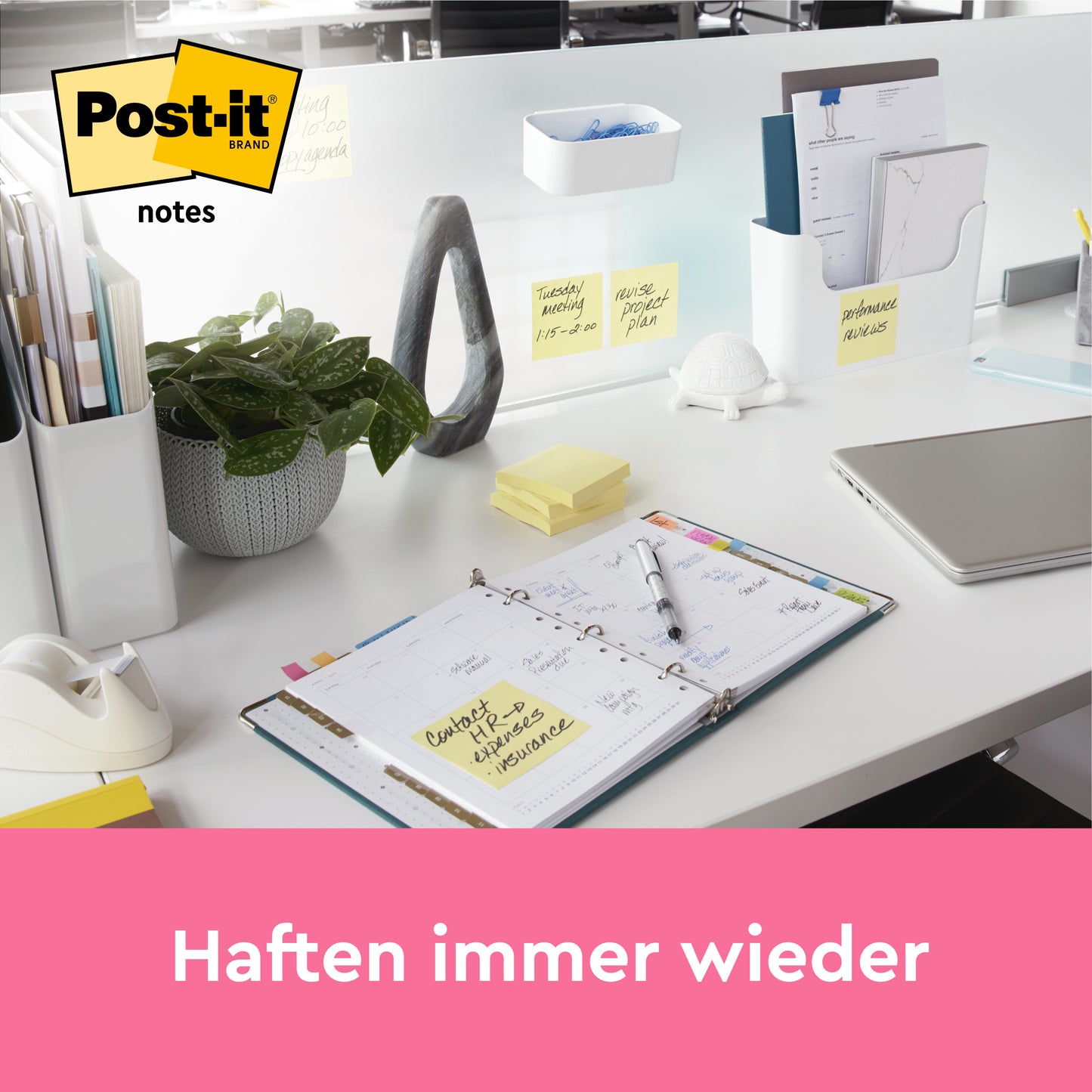 Auf einem aufgeräumten Bürotisch liegen ein offener Planer, Schreibwaren, eine Pflanze und gelbe Post-it® Notes (38 x 51 mm, 16+4 Promo Pack von 3M Deutschland GmbH) auf der Trennwand. Ein Laptop ist teilweise sichtbar. Darunter steht auf einem rosa Banner "Haften immer wieder".