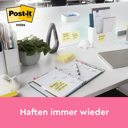 Un birou ordonat cu planificator, laptop, plantă și produse de birou precum Post-it® Notes de la 3M Deutschland GmbH (Galben, 76x127 mm, 100 foi/bloc), cu notițe galbene pe peretele despărțitor. Deasupra unei benzi roz la marginea de jos scrie "Aderă mereu din nou".